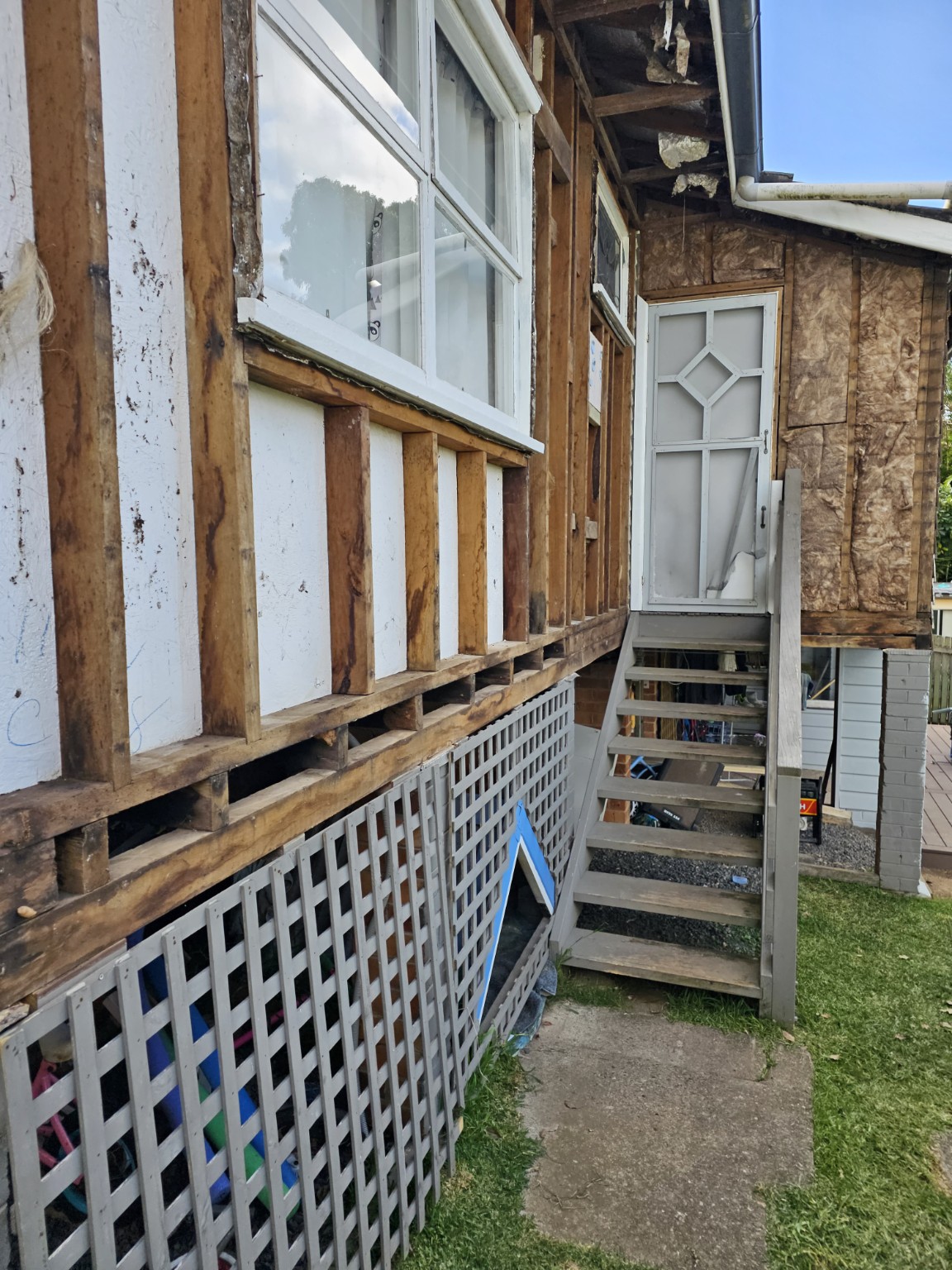 External wall framing exposed around a retained window and entry steps after sheet removal.
