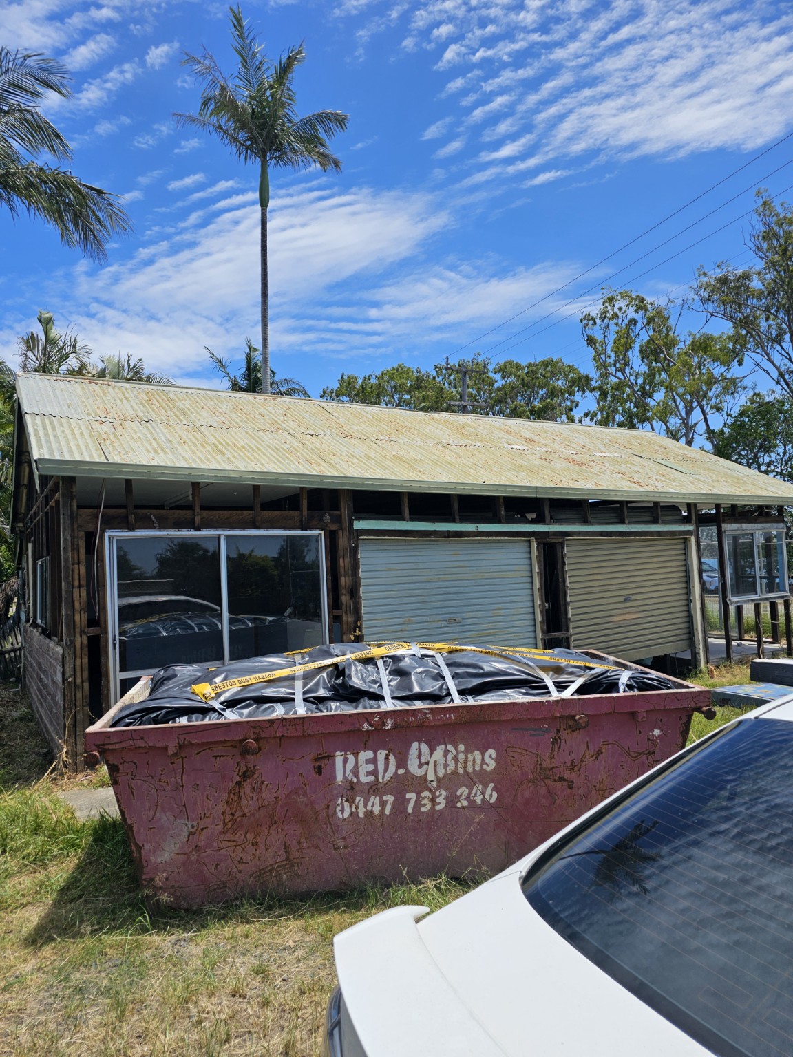 External wall removal with a covered waste skip in front of a single-storey building.