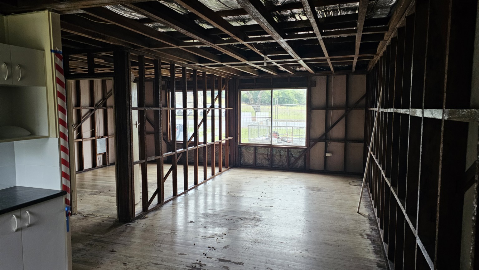 Internal walls and ceiling stripped back to timber framing beside retained kitchen cabinetry.