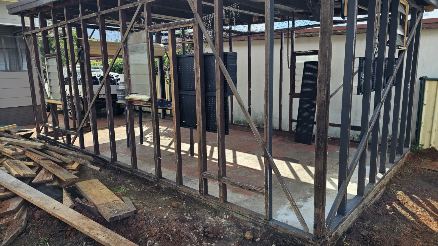 Outbuilding with external wall linings removed, leaving timber framing around a concrete floor.